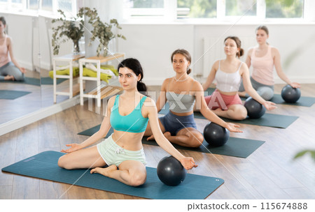 Teacher explains principle of performing body tilts and rests her hand on fitball 115674888