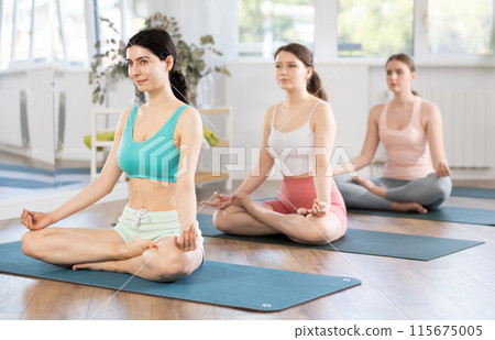 Young girl teaches yoga lesson, shows students technique of performing padmasana asana Young girl teaches yoga lesson, shows students technique of performing padmasana asana 115675005