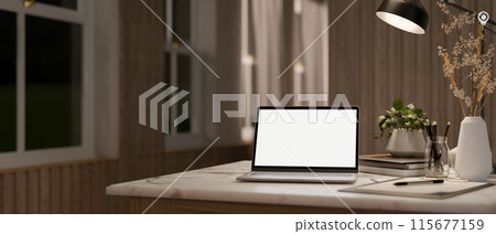 A home workspace at night, a laptop computer with a white-screen mockup on the table in a room. A home workspace at night, a laptop computer with a white-screen mockup on the table in a room. 115677159