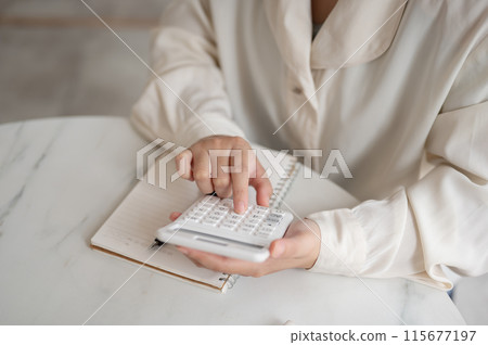 A close-up image of a woman using a calculator at a table, checking and calculating her budget. A close-up image of a woman using a calculator at a table, checking and calculating her budget. 115677197