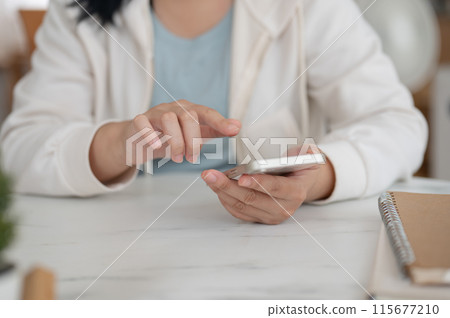 Cropped image of a woman in a hoodie sits in a cafe and uses her smartphone, scrolling on her phone. Cropped image of a woman in a hoodie sits in a cafe and uses her smartphone, scrolling on her phone. 115677210