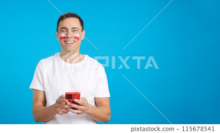 Polish supporter looking at his mobile smiling and showing it. Polish supporter looking at his mobile smiling and showing it. 115678541