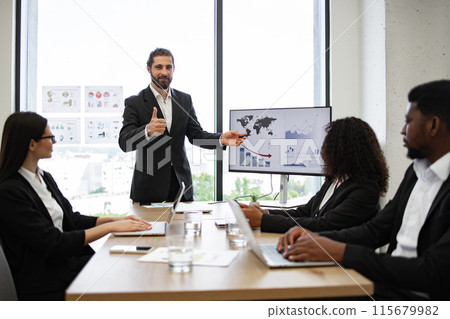 Businessman presenting to colleagues with statistical charts on screen 115679982