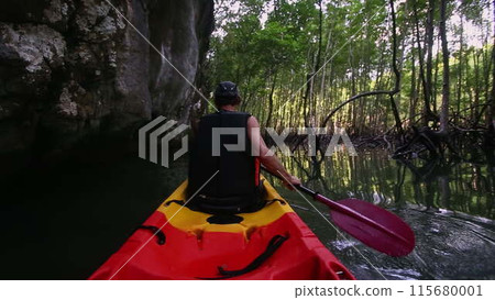 Man engages in kayaking close to cliff passing tree branches 115680001