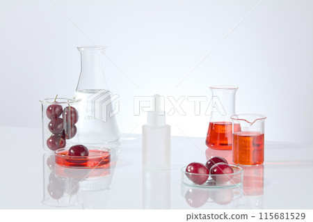 Cosmetic advertising mockup on white background, decorated with fresh cherry and lab items. Red and transparent liquid filled in glassware, blank label cosmetic bottle displayed in center Cosmetic advertising mockup on white background, decorated with fresh cherry and lab items. Red and transparent liquid filled in glassware, blank label cosmetic bottle displayed in center 115681529