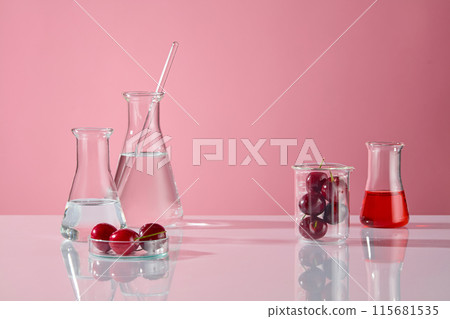 White table contains some erlenmeyer flask of transparent liquid on the left, a beaker of fresh cherry fruit and red liquid erlenmeyer flask on the right, vacant space in center for product displaying White table contains some erlenmeyer flask of transparent liquid on the left, a beaker of fresh cherry fruit and red liquid erlenmeyer flask on the right, vacant space in center for product displaying 115681535