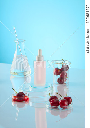 An unlabeled cosmetic bottle displayed on two glass podiums stack of each others, around it is a transparent fluid erlenmeyer flask, a dish of red liquid, petri dish and beaker contains ripe cherries 115681575