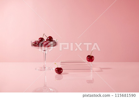 A cocktail glass containing ripe cherries and an empty glass pedestal placed side by side on the table, over pastel pink background. Many blank spaces around for designing and adding text A cocktail glass containing ripe cherries and an empty glass pedestal placed side by side on the table, over pastel pink background. Many blank spaces around for designing and adding text 115681590