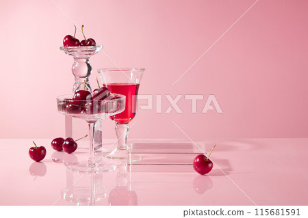 Variety glass including cocktail glass of fresh cherry and wine glass filled by red liquid placed together on the table, a rectangular platform of glass beside, over pink background 115681591