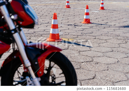 Close up of motorcycle part with orange cones on motordrome on background. Concept of motorcycle school of driving. Riding between cones, lesson in motorcycle school. Nobody 115681680