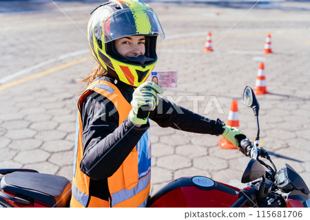 Female student L driver wearing protect orange vest showing motorcycle driving license as successfully finished riding exams. 115681706