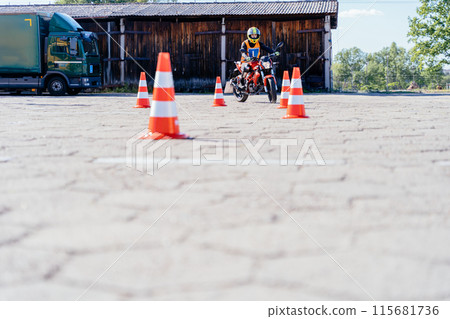 L-driver female driver with helmet taking motorcycle lessons and practicing ride. slalom through the orange cones on motordrome on motorcycle. Motorcycle school of driving. 115681736