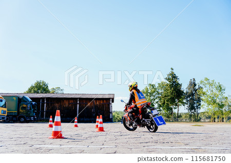 L-driver female driver with helmet taking motorcycle lessons and practicing ride. slalom through the orange cones on motordrome on motorcycle. Motorcycle school of driving. 115681750