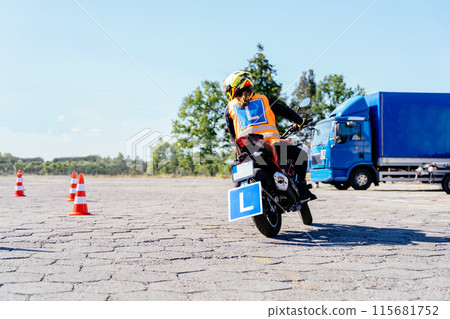 L-driver female driver with helmet taking motorcycle lessons and practicing ride. slalom through the orange cones on motordrome on motorcycle. Motorcycle school of driving. 115681752