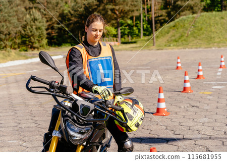 Learning to ride motorcycle concept. Female L-driver relax after driving between cones, lesson in motorcycle school. 115681955