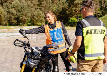 A woman in a motorcycle safety vest is being instructed by a man instructor of driving school in bright yellow vest. Concept of learning and guidance 115681956