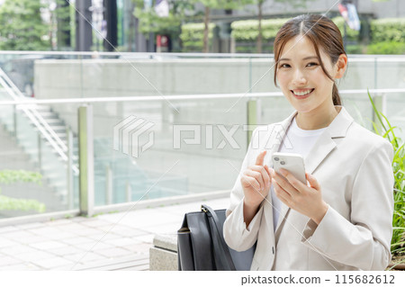A young woman sitting on a bench and searching on her smartphone A young woman sitting on a bench and searching on her smartphone 115682612