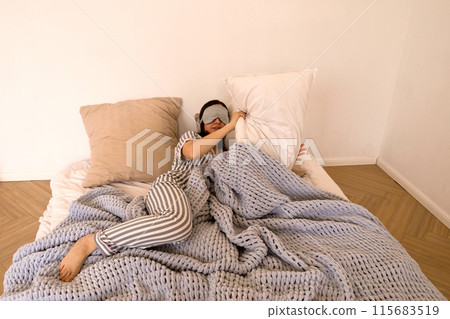 Woman lying in bed covering eyes with eye mask. 115683519
