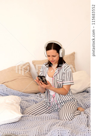 Woman reacting to smartphone content with headphones in bed. 115683552