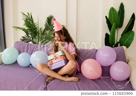Girl laughing with party hat and holding birthday gifts. 115683900
