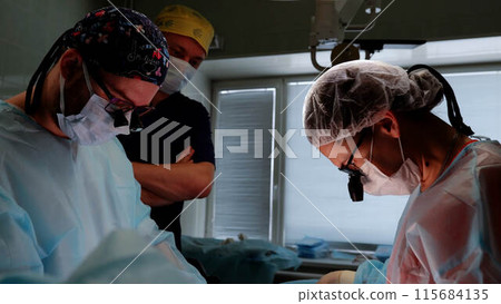 In operating room team of doctors and assistants focuses on performing microsurgery to save patient's life. Modern medicine advanced technologies and expertise of professionals saving lives. 115684135