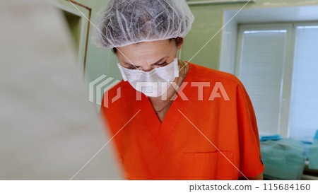 Surgical team led by female surgeon perform delicate procedure in modern hospital setting. Collaboration precision required in medical hospital advancements and expertise within modern surgery. 115684160