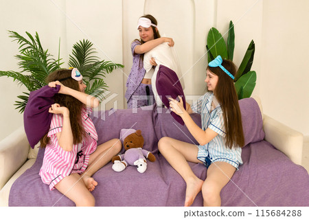 Sisters playfully hugging and laughing on the couch. Sisters playfully hugging and laughing on the couch. 115684288