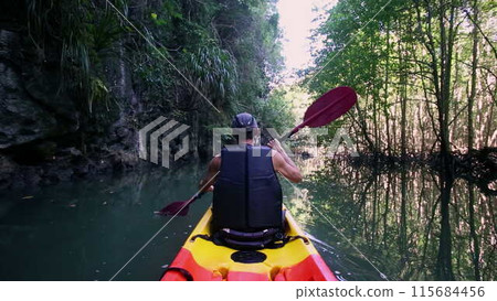 Man sails kayak in calm river surrounded by cliff and trees 115684456