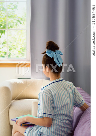 Teenage girl in striped pajamas reading near window 115684462