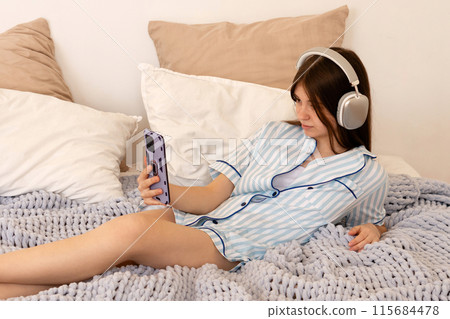 Teenager relaxing on bed with headphones and smartphone. 115684478