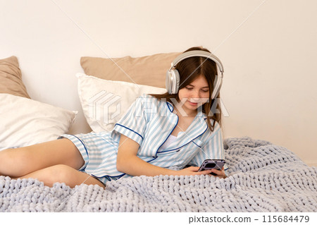 Teenage girl lying on bed using smartphone and headphones 115684479