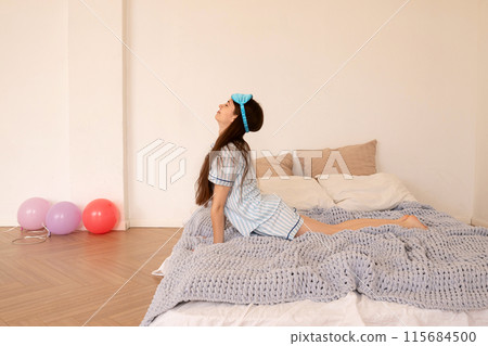 Teenage girl stretching and looking upwards while sitting in bed. Teenage girl stretching and looking upwards while sitting in bed. 115684500