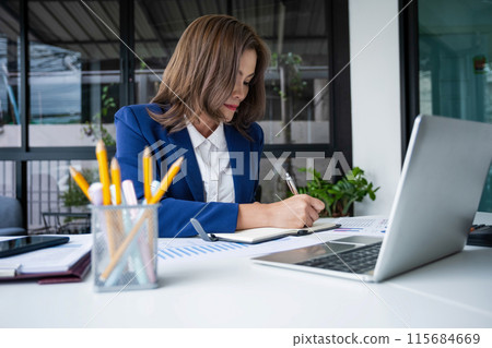 a young girl sits at a table in the office and holds a pen and works with documents 115684669