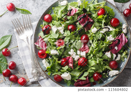 Salad with ripe cherries, arugula, radicchio and feta cheese dressed with balsamic dressing close-up in a plate. Horizontal top view 115684802