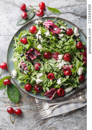 Summer salad with berries cherry, arugula, chicory and feta cheese dressed with balsamic sauce close-up in a plate. Vertical top view 115684806