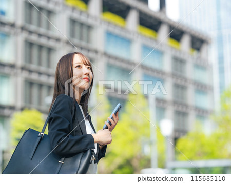 A female business person using a smartphone on a street corner 115685110