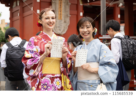 一個穿著和服、很高興看到財富的外國女人和一個引導她的日本女人 一個穿著和服、很高興看到財富的外國女人和一個引導她的日本女人 115685539