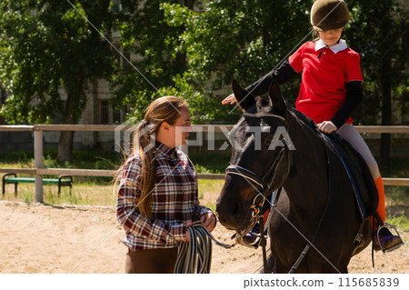 Instructor discusses technique with young rider during equestrian lesson. Instructor discusses technique with young rider during equestrian lesson. 115685839