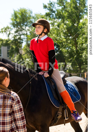 Rider on horse receiving instruction in sunlight. 115685843