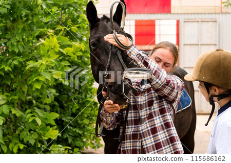 Woman adjusting bridle on horse while interacting with rider. Woman adjusting bridle on horse while interacting with rider. 115686162