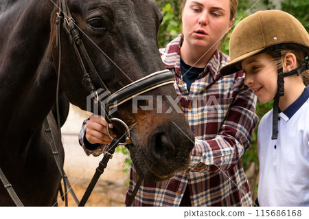 Woman teaching young rider to adjust horse's bridle. Woman teaching young rider to adjust horse's bridle. 115686168