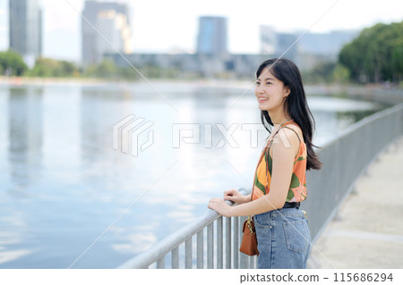 A joyful urban escape by the lake, a young woman in an orange shirt enjoys nature 115686294