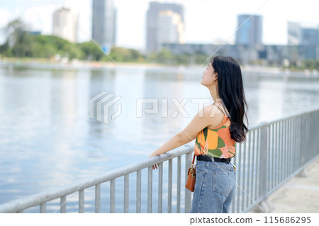 The joy of conversation by the waterfront, a young woman in an orange shirt basks in the beauty of outdoors. The joy of conversation by the waterfront, a young woman in an orange shirt basks in the beauty of outdoors. 115686295