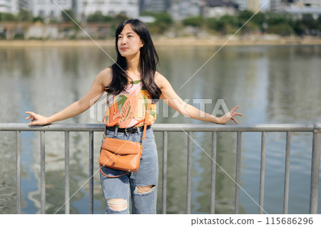 A portrait of joy a pretty lady in an orange shirt talks on the phone, bathed in sunlight by the lake. 115686296