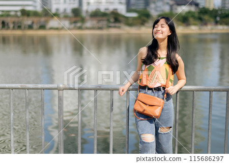 A portrait of joy, a pretty lady in an orange shirt talks on the phone, bathed in sunlight by the lake. A portrait of joy, a pretty lady in an orange shirt talks on the phone, bathed in sunlight by the lake. 115686297