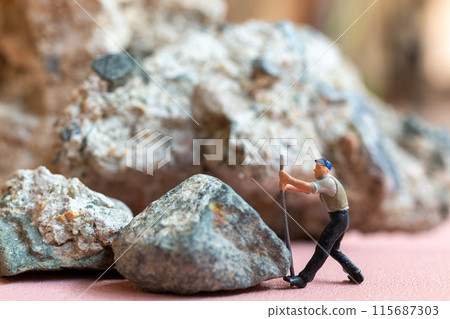 Miniature worker pushing a large rock. Themes of perseverance, strength and labor. This makes it suitable for use in content that involves hard work, challenges, and overcoming obstacles. 115687303