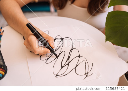 Lady draws with a black felt-tip pen on a white sheet 115687421