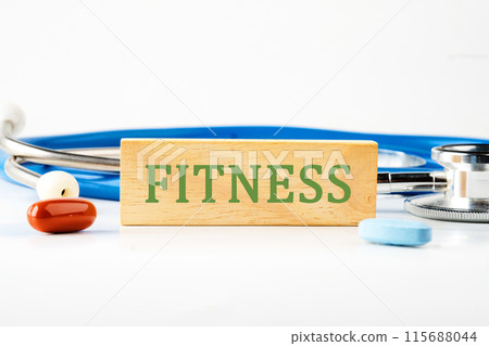 Fitness, healthy lifestyle concept. A word FITNESS written on a wooden bar in front of a stethoscope next to pills, vitamins Fitness, healthy lifestyle concept. A word FITNESS written on a wooden bar in front of a stethoscope next to pills, vitamins 115688044
