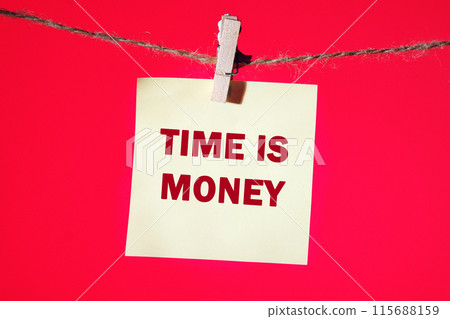 Stock market concept,TIME IS MONEY written on a yellow sticker suspended from a rope in front of a red background Stock market concept,TIME IS MONEY written on a yellow sticker suspended from a rope in front of a red background 115688159