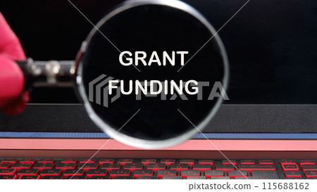 Business and grant funding concept. Copy space. Words GRANT FUNDING text appeared through a magnifying glass on a dim laptop screen 115688162